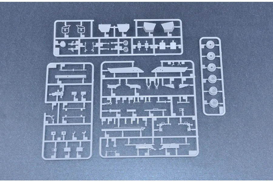 Three grey plastic model kit sprues containing various vehicle parts laid out on a dark surface.