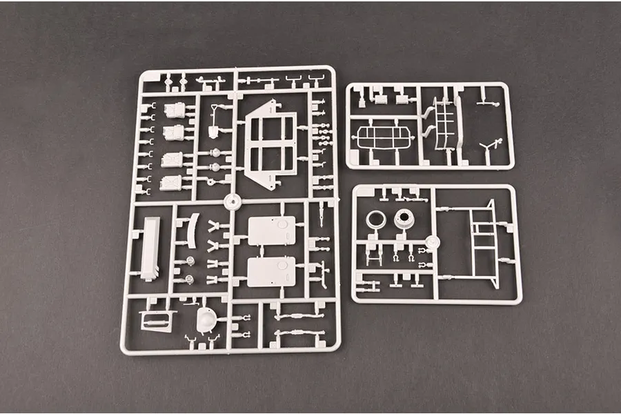 Three grey plastic model kit sprues containing various vehicle parts laid out on a dark grey surface.