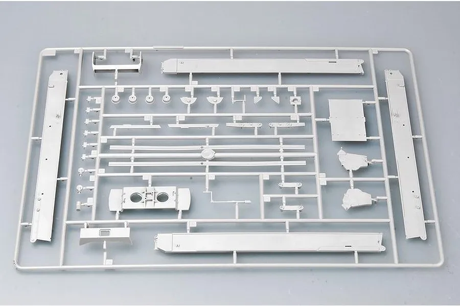 A grey plastic sprue containing various model kit parts for a 1/35 scale military vehicle, including long side panels and small mechanical components.