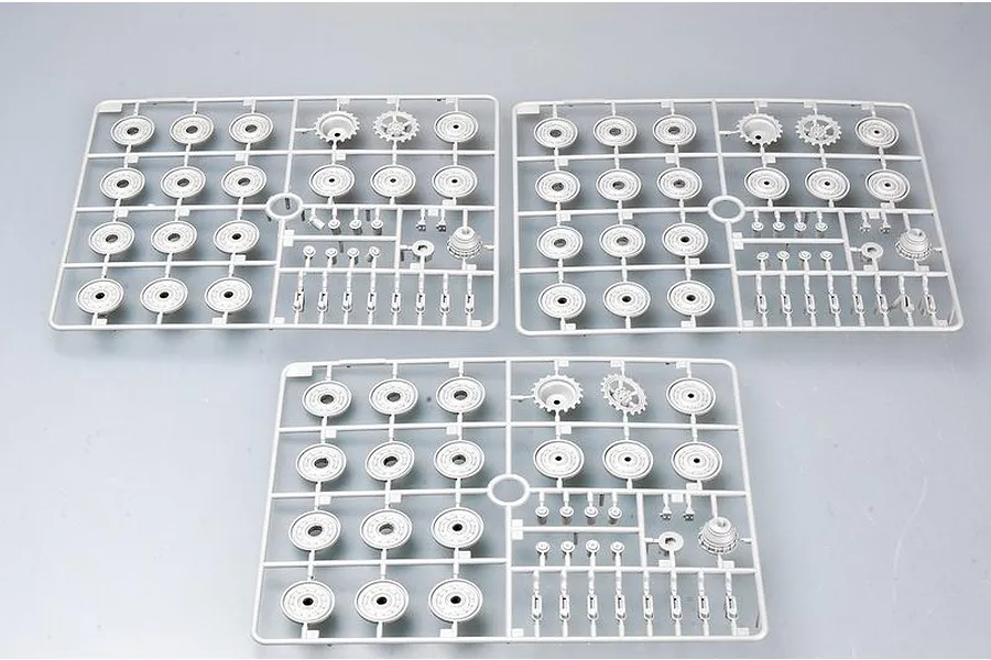 Three identical grey plastic model kit sprues containing tank road wheels and sprockets on a plain light grey background.