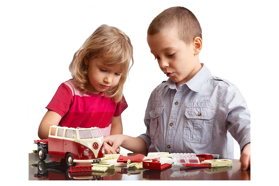 A young boy and girl sitting at a table assembling a red and white Airfix Quickbuild Volkswagen Kombi model van.