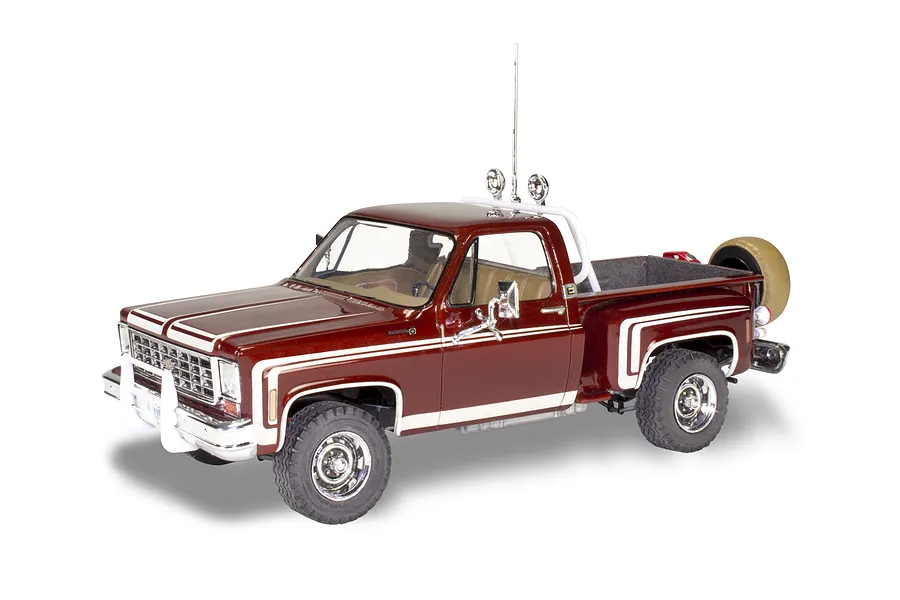 A 1/24 scale model of a 1976 Chevrolet Stepside pickup truck, painted deep red with white racing stripes, featuring a roll bar, off-road lights, and spare tire.