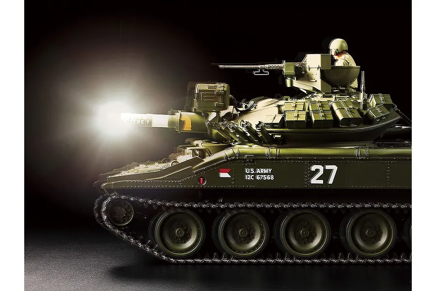 Side view of a Tamiya 1/16 scale M551 Sheridan RC tank model with a bright light effect at the end of the main gun barrel against a black background.