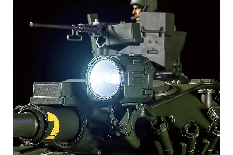 Close-up of a Tamiya 1/16 scale M551 Sheridan RC tank showing the illuminated spotlight on the turret and a commander figure in the background.