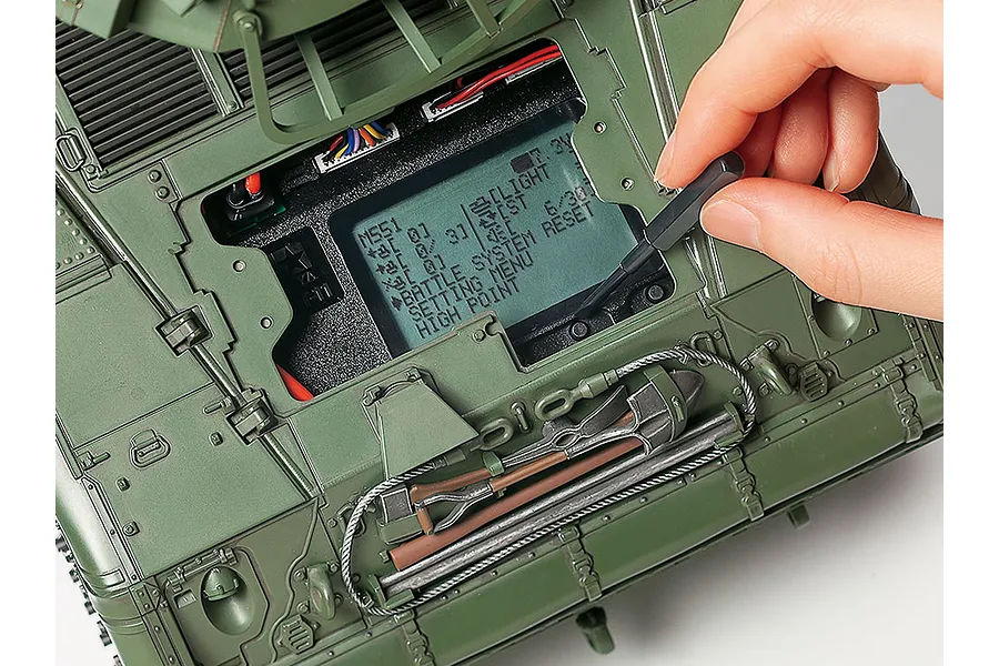 A person using a small tool to adjust settings on the digital display screen of a Tamiya 1/16 scale M551 Sheridan RC tank.