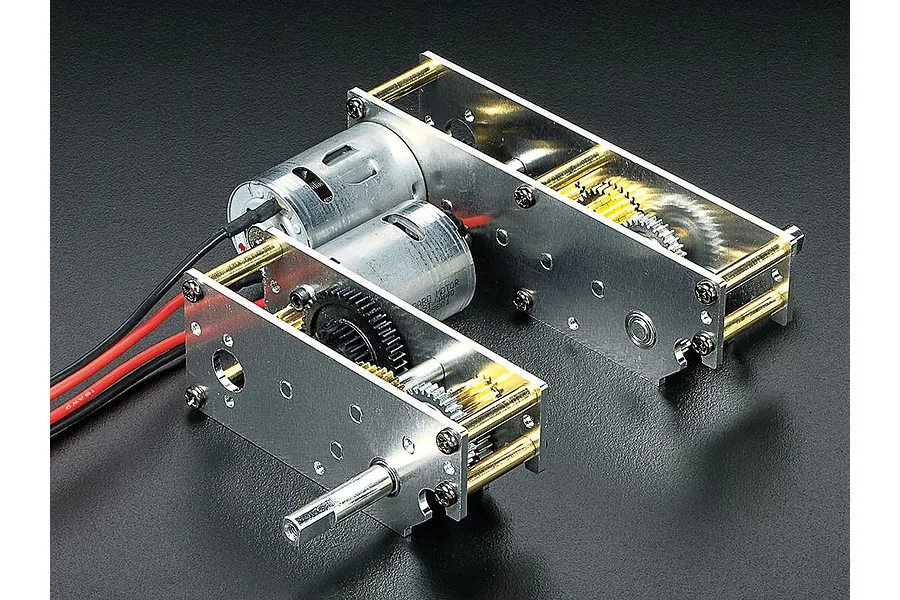 A Tamiya RC tank dual motor gearbox assembly with metal plates, brass spacers, and exposed gears on a black background.