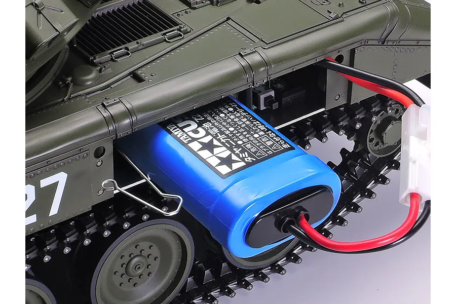 A Tamiya 1/16 scale RC tank with its side panel open, showing a blue Tamiya 7.2V battery pack installed inside the chassis.