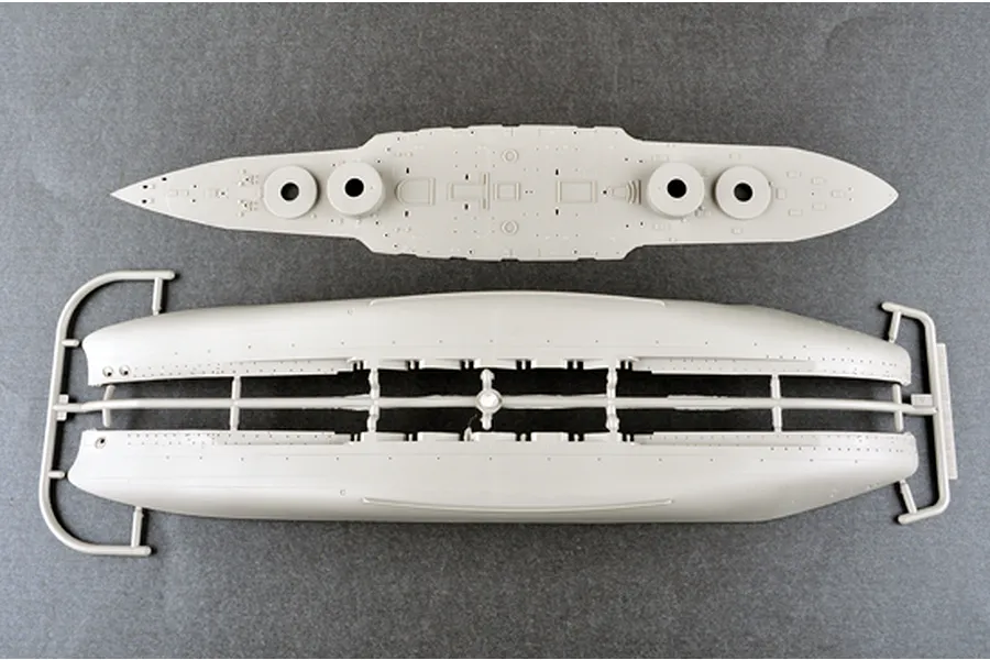 Top-down view of unpainted plastic model ship parts including the main deck and hull halves on a grey background.