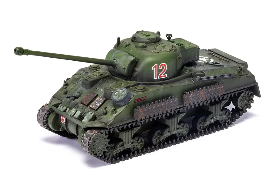 A painted 1/72 scale plastic model of a Sherman Firefly tank, featuring olive green camouflage, the number 12 on the turret, and weathering effects.