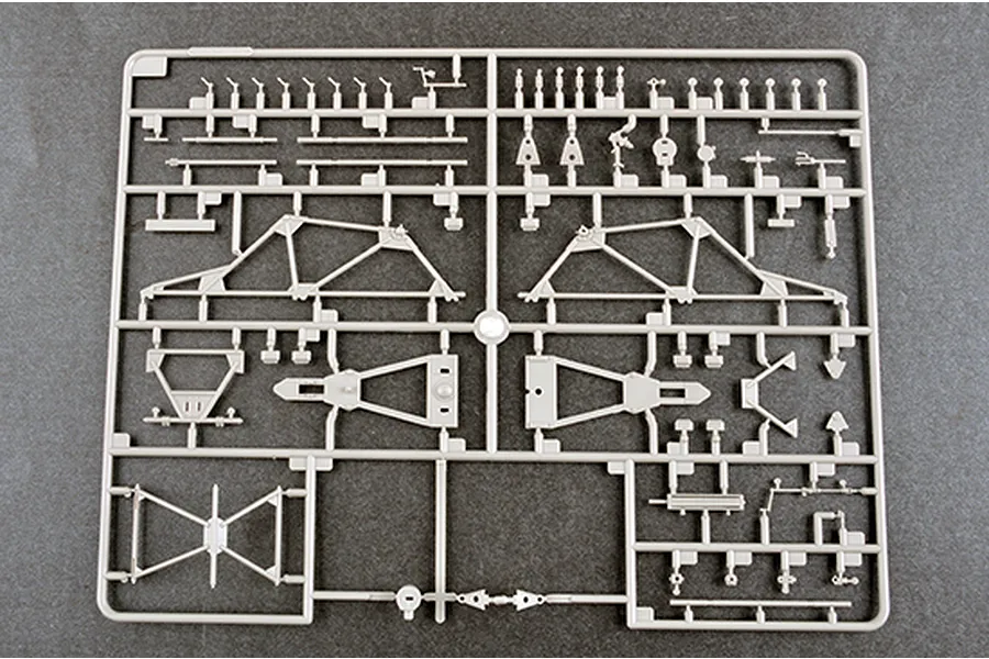 A grey plastic sprue containing various model kit parts for a military vehicle, including frame components and small mechanical details.