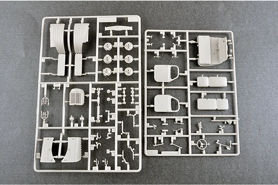 Two light grey plastic model kit sprues containing various vehicle parts like fenders, doors, and interior components on a grey background.