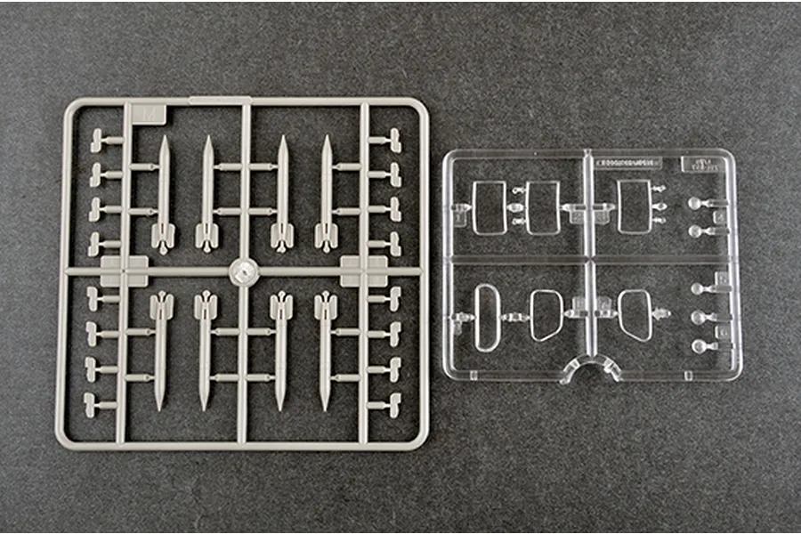Two plastic model kit sprues on a dark grey background, one with grey rocket parts and one with clear plastic window or lens parts.