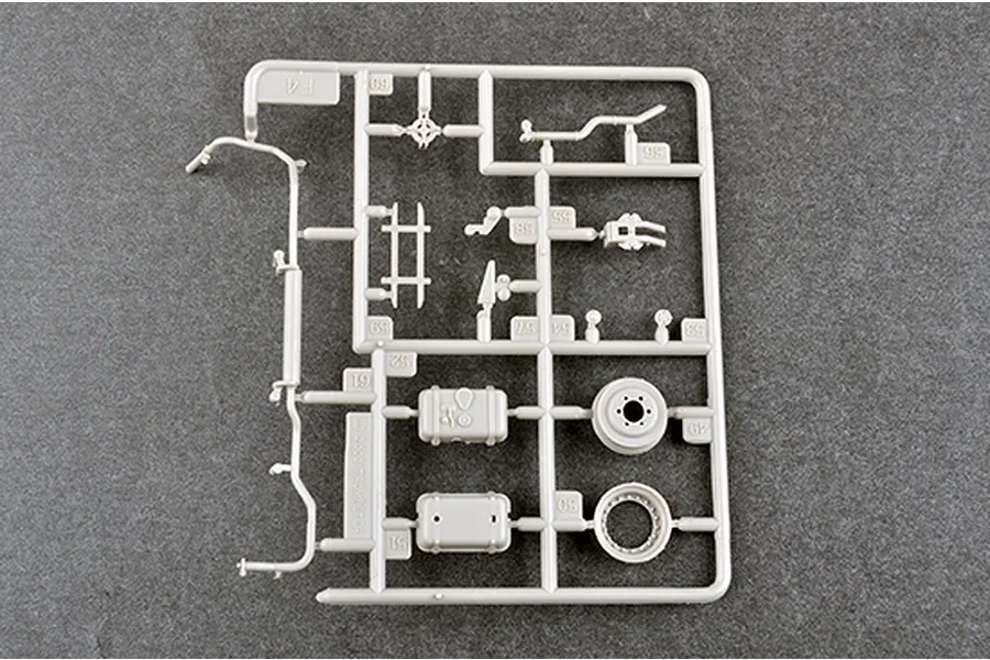 A grey plastic model kit sprue labeled F4 containing various small vehicle parts, including wheels and storage boxes, on a dark grey surface.