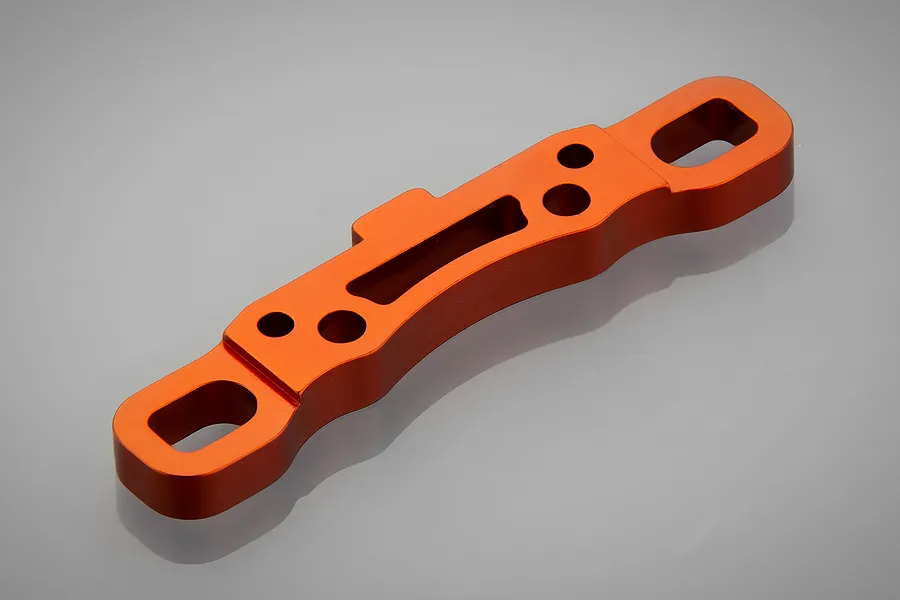An orange anodized aluminium suspension arm pin mount for an RC car, shown from an angled top-down perspective on a grey background.