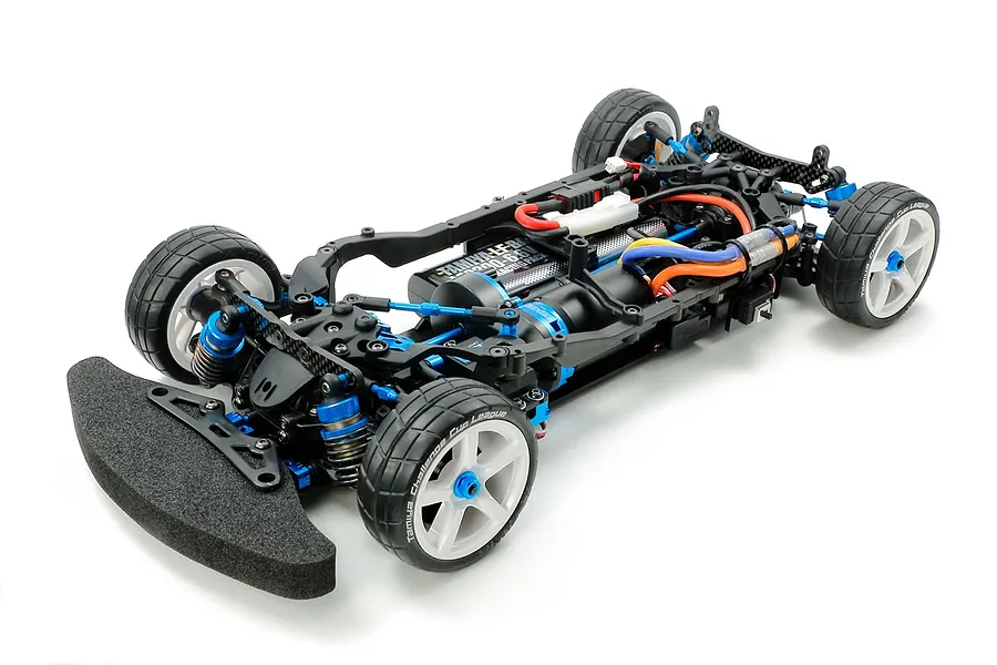 A high-angle studio shot of a Tamiya TB-05R 1/10 scale RC touring car chassis, featuring blue anodized aluminum parts, carbon fiber shock towers, and foam bumper.