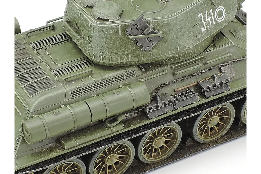Close-up of a Tamiya 1/48 scale T-34/85 tank model showing the turret, hull, and road wheels with olive green paint and white markings.