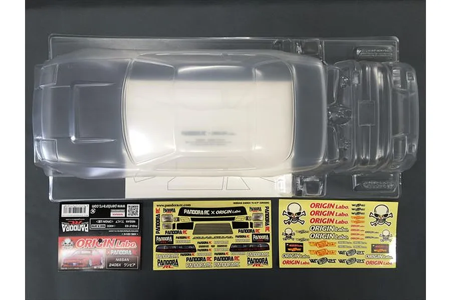 Unpainted clear polycarbonate RC car body shell for a Nissan One-Via with decal sheets and packaging on a dark surface.