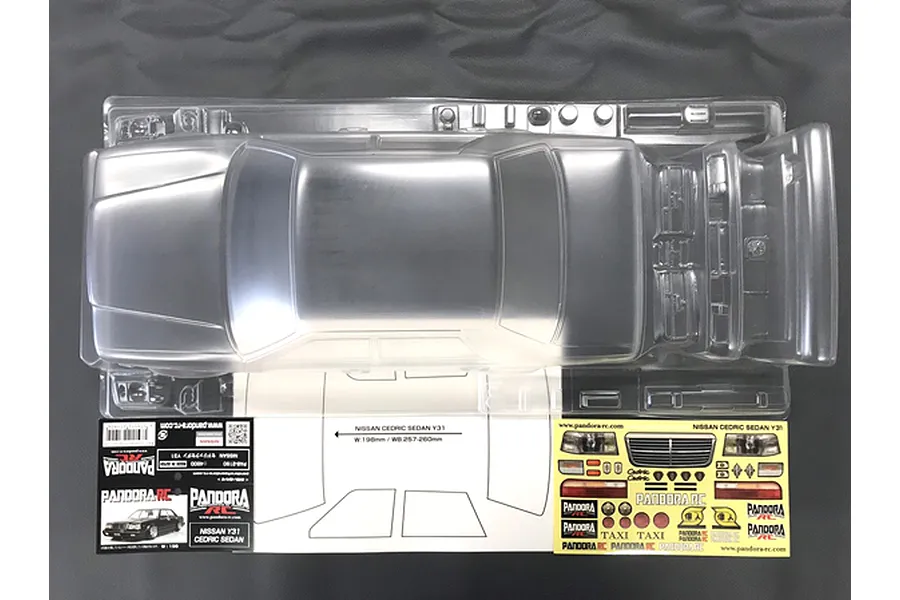 Top-down view of an unpainted clear polycarbonate RC car body shell for a Nissan Y31 Cedric Sedan, including decals and window masks in packaging.