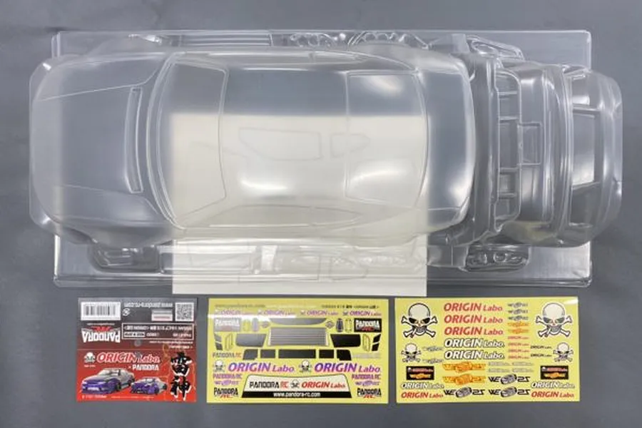 Top-down view of an unpainted clear polycarbonate RC car body shell for a Nissan Silvia S15, including decal sheets and packaging inserts.