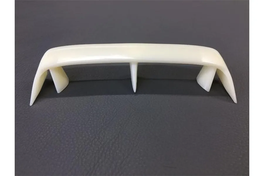 An unpainted white plastic RC car rear wing spoiler with a central support strut, viewed from the front against a dark grey textured background.