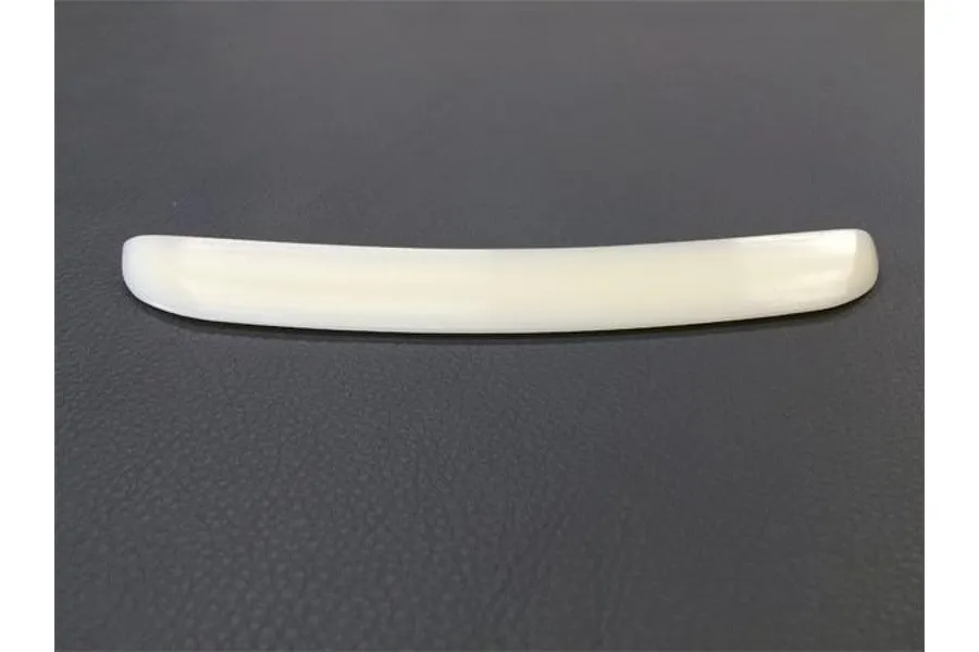 A curved, unpainted white plastic RC car rear wing spoiler sitting on a dark grey textured surface.