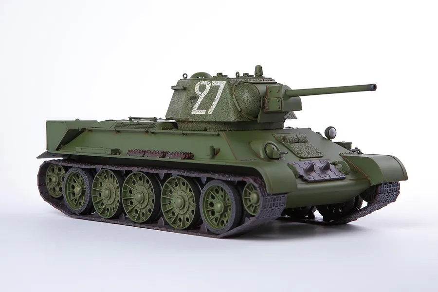 A side-angle view of a 1/35 scale Academy USSR T-34/76 tank model, painted in olive green with the number 27 on the turret, set against a white background.