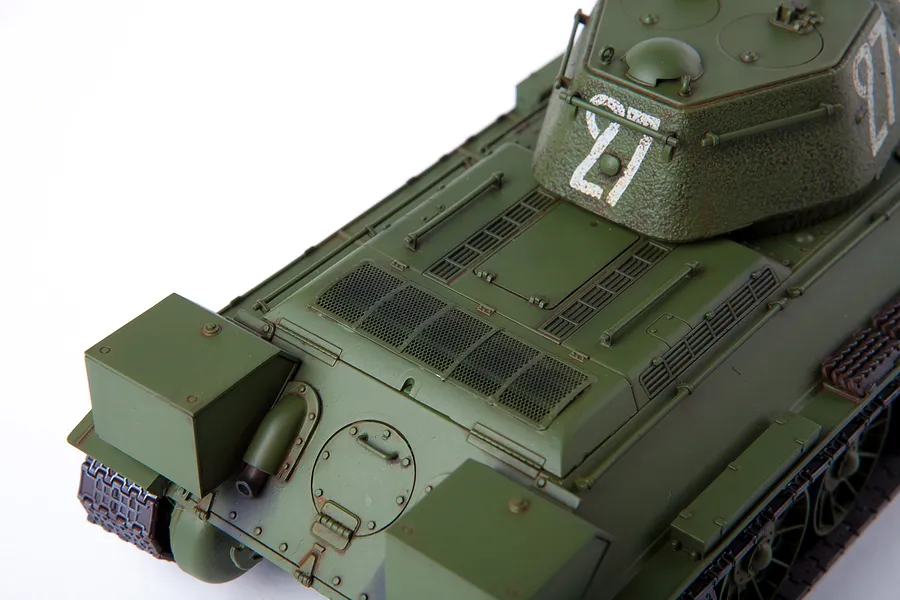 A high-angle close-up view of an assembled and painted olive green T-34/76 tank model kit on a white background.