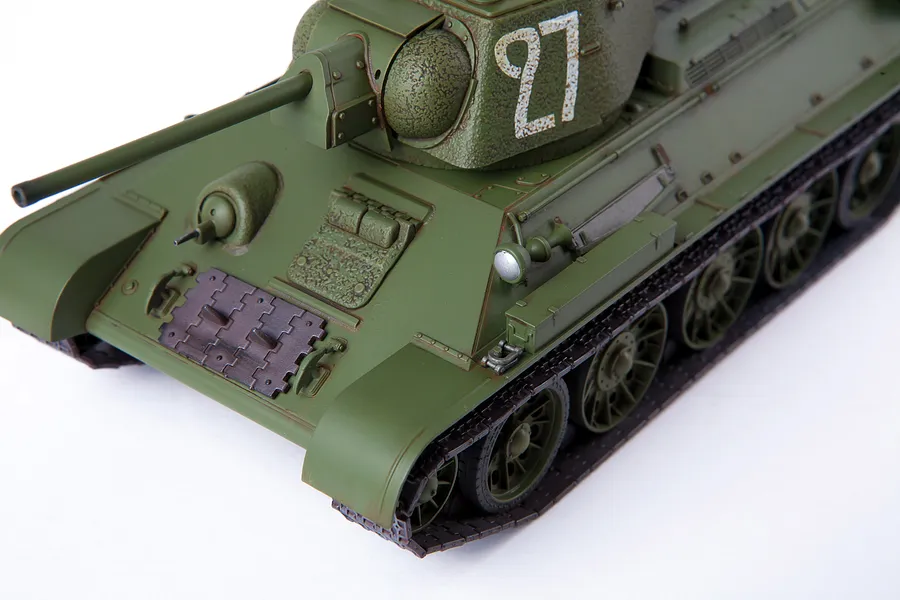 A high-angle close-up of a 1/35 scale Academy T-34/76 tank model, painted olive green with the number 27 on the turret.