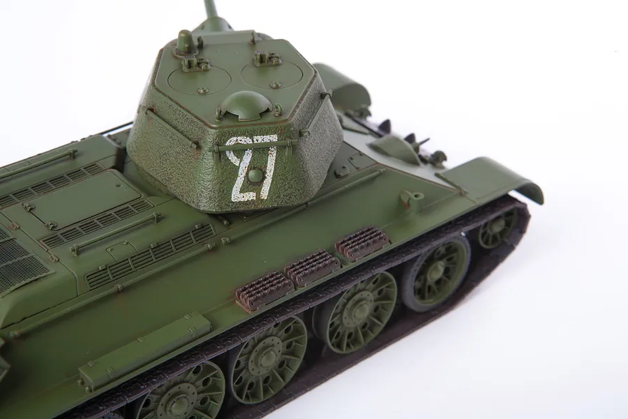 A high-angle studio shot of a 1/35 scale plastic model of a Soviet T-34/76 tank, painted in olive green with the number 27 on the turret.