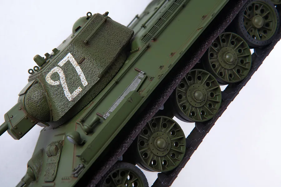 A close-up, high-angle view of an assembled and painted 1/35 scale T-34/76 tank model, showing the turret with number 27 and the road wheels.