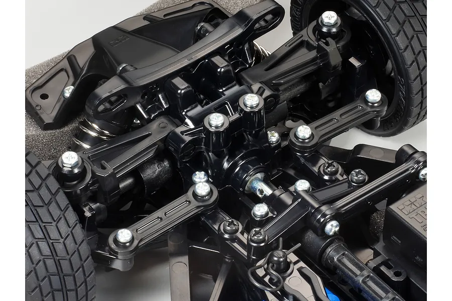 Close-up of the front suspension and steering assembly of a Tamiya TT-02 RC car chassis, showing black plastic components and metal screws.