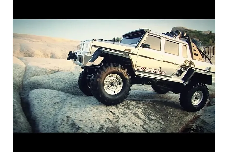 A silver Killerbody Horri-Bull RC crawler body shell mounted on a chassis, driving over light-coloured rocky terrain.
