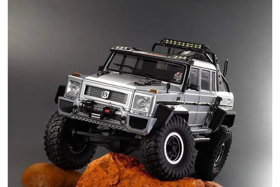 A silver Killerbody Horri-Bull RC crawler body shell mounted on a chassis, positioned on orange rocks against a grey background.