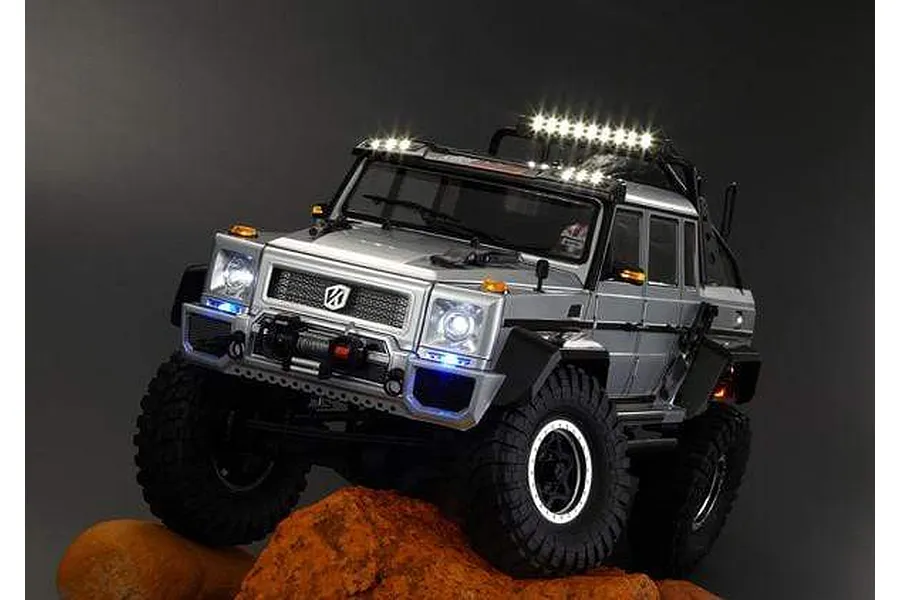 A silver Killerbody Horri-Bull 1/10 scale RC crawler body shell with working LED lights, positioned on a rock against a dark background.
