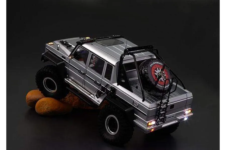 A silver Killerbody Horri-Bull RC crawler body shell mounted on a chassis, posed on rocks against a dark background.