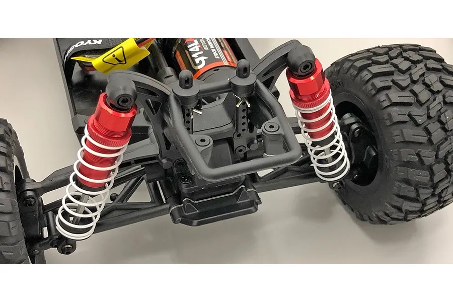 Close-up of the rear suspension of a Kyosho RC car featuring red aluminium shock absorbers with white springs installed on a black chassis.