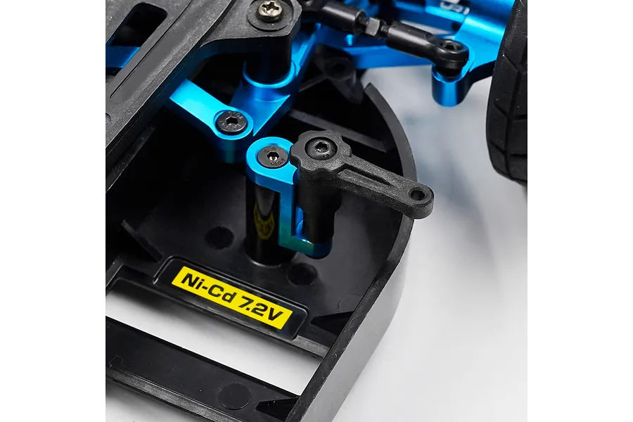 Close-up of a blue aluminium battery mount installed on an RC car chassis with a black plastic battery retainer arm.