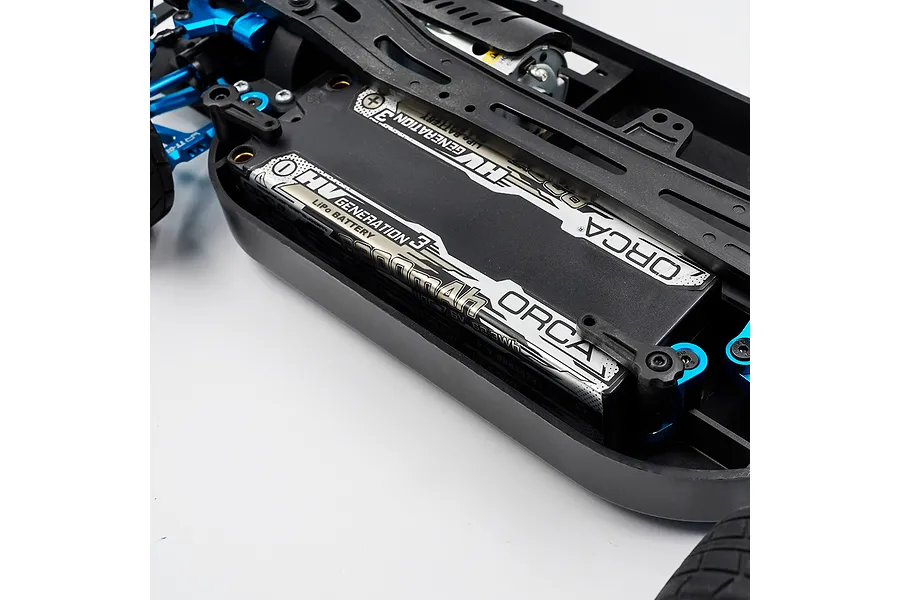 Close-up of a blue aluminium battery mount installed on an RC car chassis holding an Orca LiPo battery.