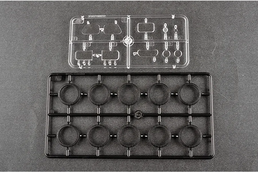 Two plastic model kit sprues on a grey background, one clear with small parts and one black with ten circular wheel-like components.