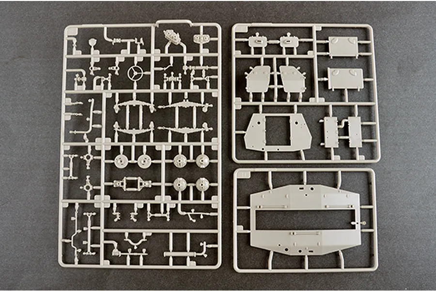 Three grey plastic model kit sprues containing various vehicle parts for a 1/35 scale military model kit on a dark grey background.