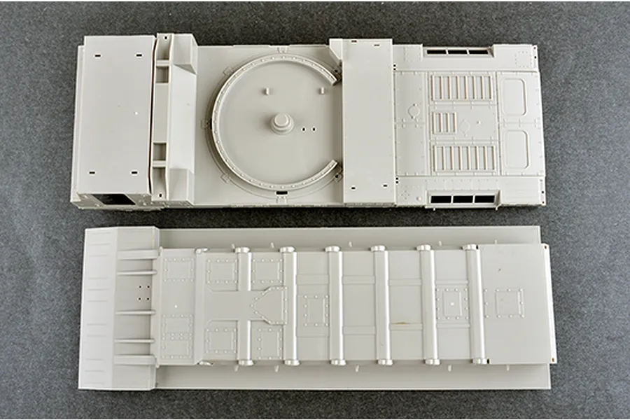 Top-down view of two unpainted plastic model kit parts for a military vehicle, showing the main chassis and lower hull sections.
