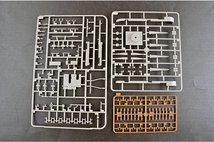 Three plastic model kit sprues containing various grey and tan ship parts laid out on a dark grey surface.