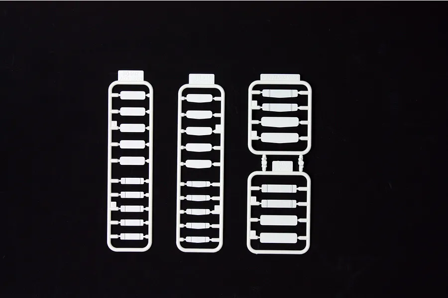 Three white plastic model kit sprues containing various small rectangular parts on a black background.