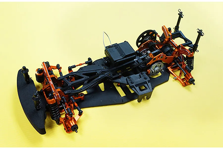 A partially assembled HPI Sprint 2 RC car chassis featuring orange anodized aluminium upgrade parts on a yellow background.