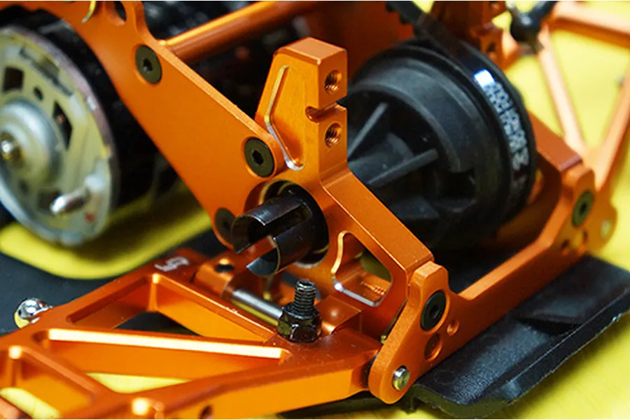 Close-up of orange anodized aluminium RC car chassis parts installed on an HPI Sprint 2, showing suspension arms and drivetrain components.