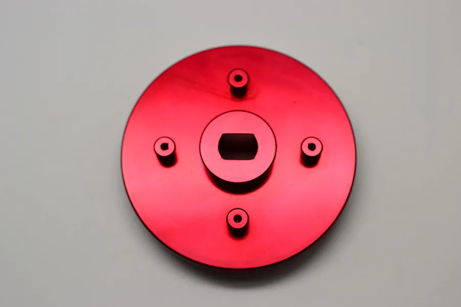 A red anodized aluminium spur gear adapter for HPI Baja 5B RC cars, featuring a circular plate with a central mounting hole and four smaller screw posts.