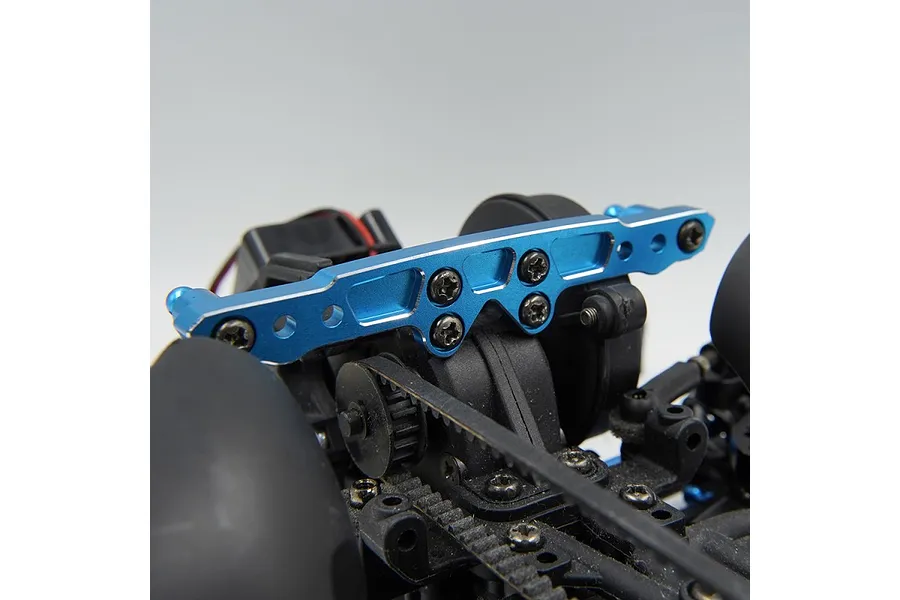 A blue anodized aluminium RC shock tower installed on a black RC car chassis, showing mounting holes and screw hardware.