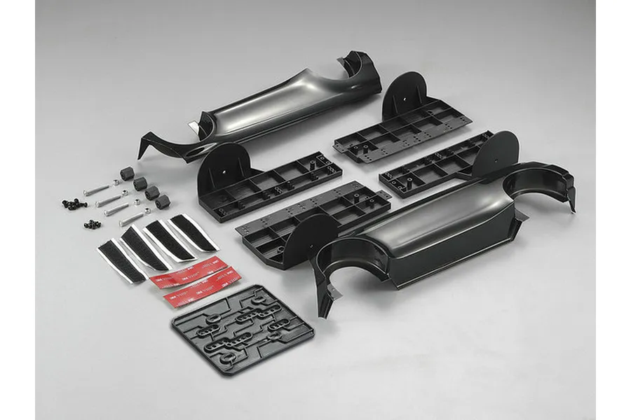 Killerbody 1/10 scale display chassis kit components including black plastic frame parts, screws, adhesive strips, and mounting hardware on a grey background.