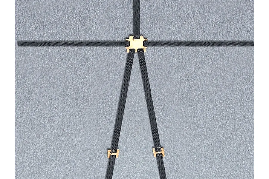 A black RC scale model safety harness with gold-coloured metal buckles laid out on a grey surface.