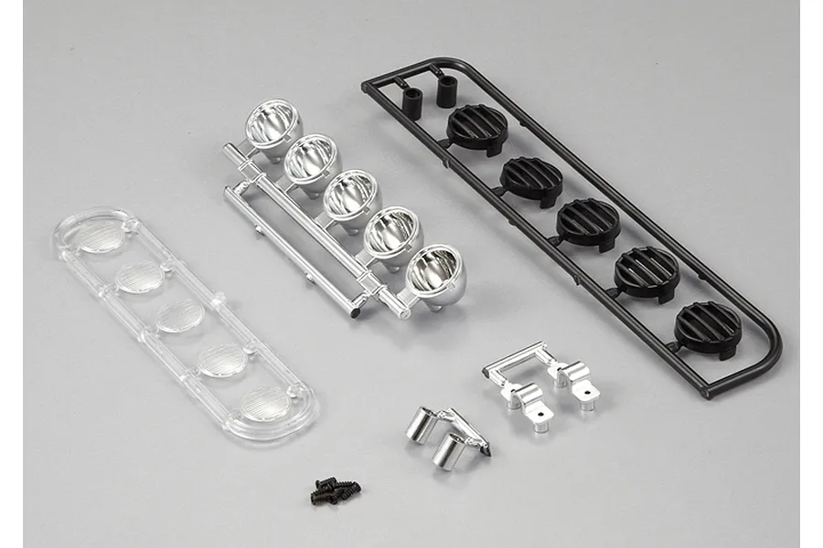 A set of unassembled RC truck roof light parts including chrome reflectors, black light covers, clear lenses, and small screws on a grey background.